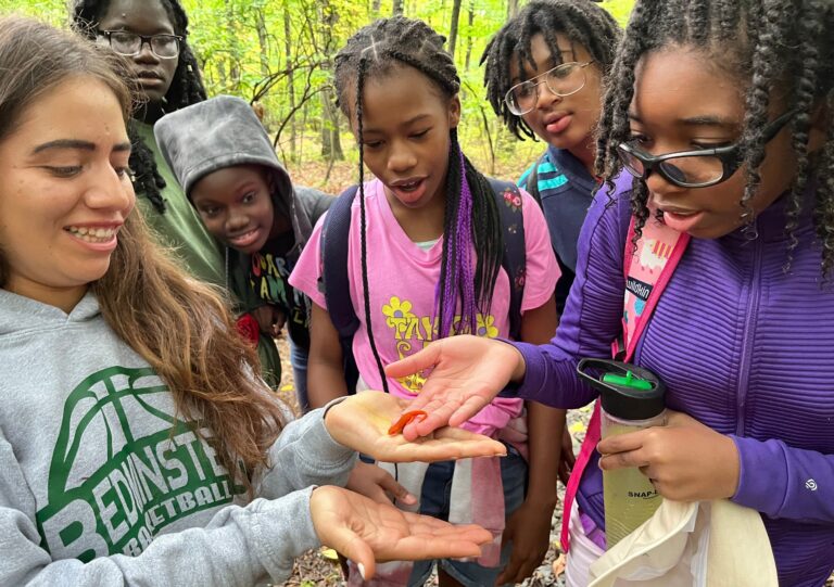photo of a group of middle school girls outdoors looking at a small lizard one of them is holding