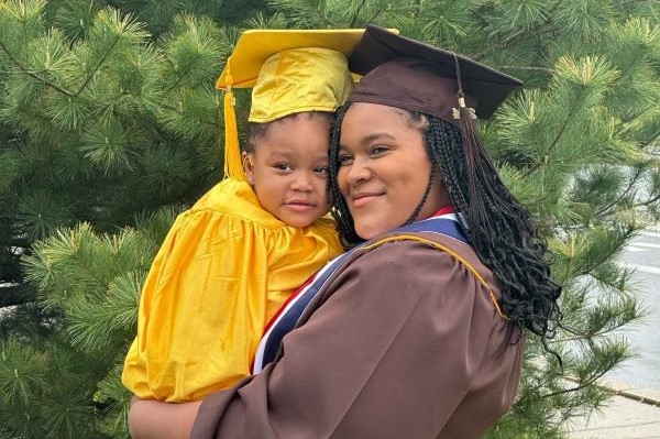 College graduate holding her 2-year-old, also in cap and gown