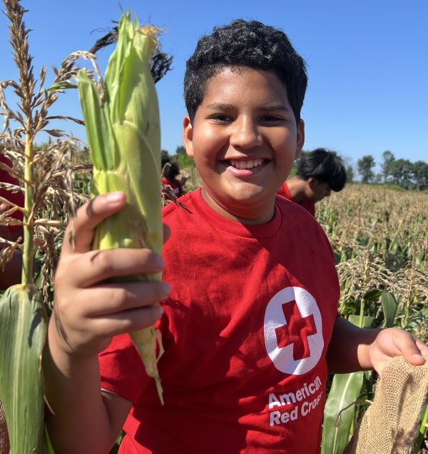 Teen holding an ear of corn with a corn field in the background