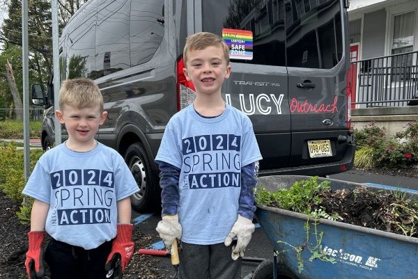 two children posing in front of van with wheelbarrow of weeds removed from garden