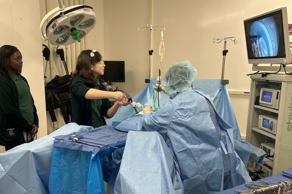 teen girl conducts mock surgery while a medical professional helps.