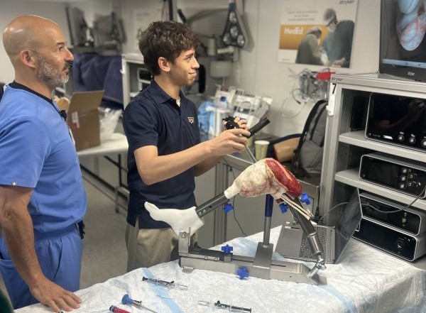 teen boy manipulates a model of a knee while a doctor looks on